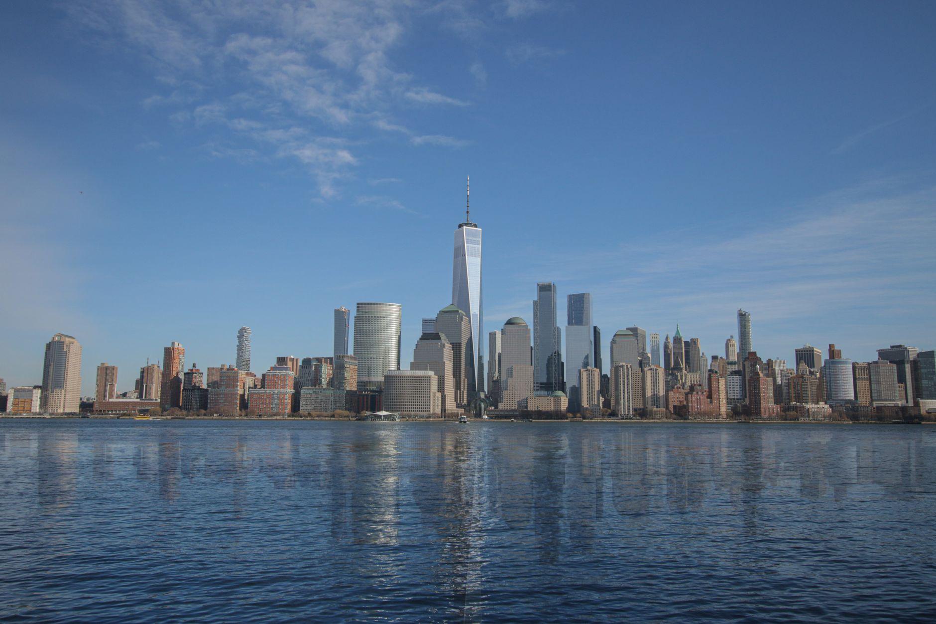 Stunning view of the New York City skyline featuring One World Trade Center reflected in water.