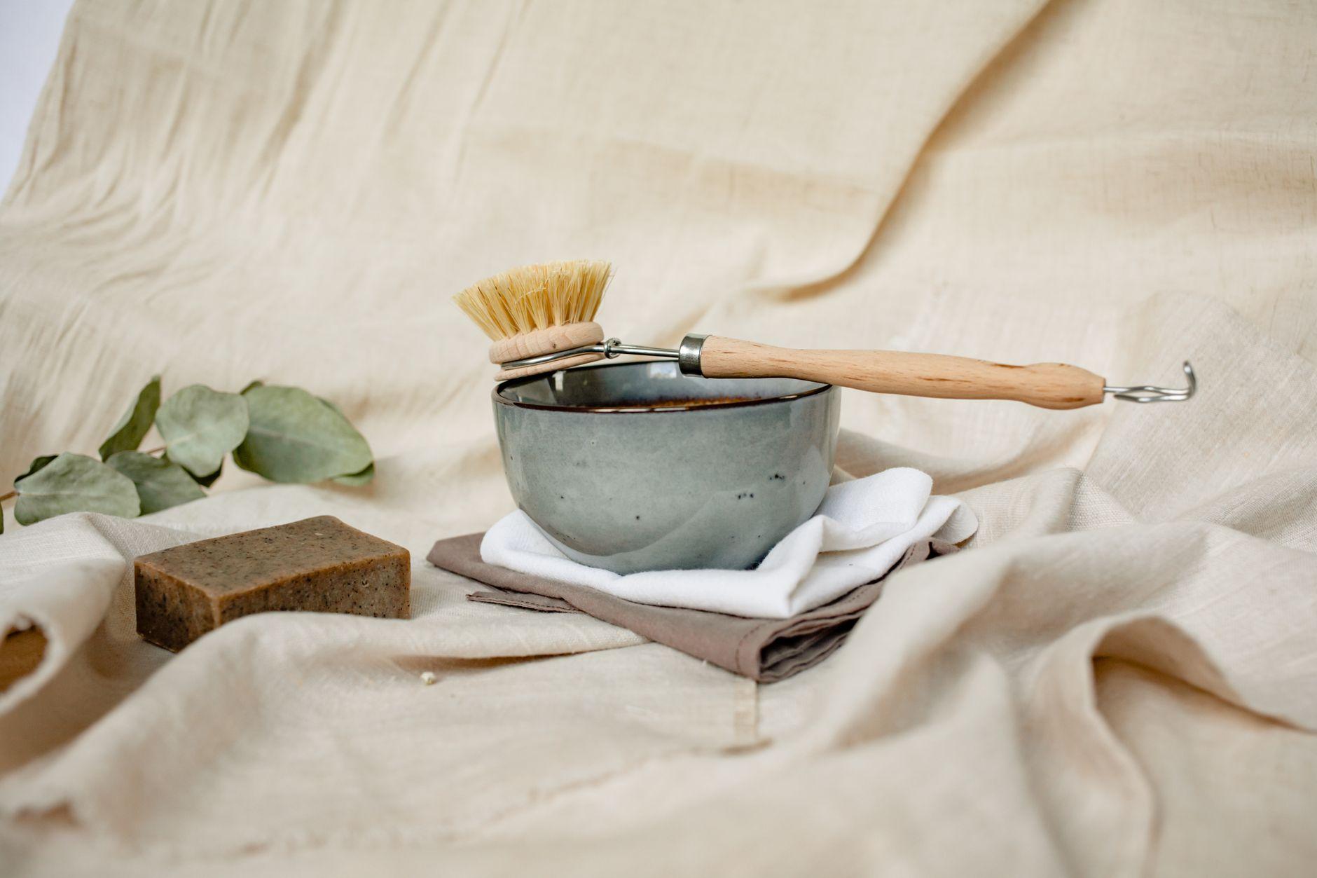 Eco-friendly cleaning set featuring a ceramic bowl, brush, soap, and natural linens with eucalyptus leaves.