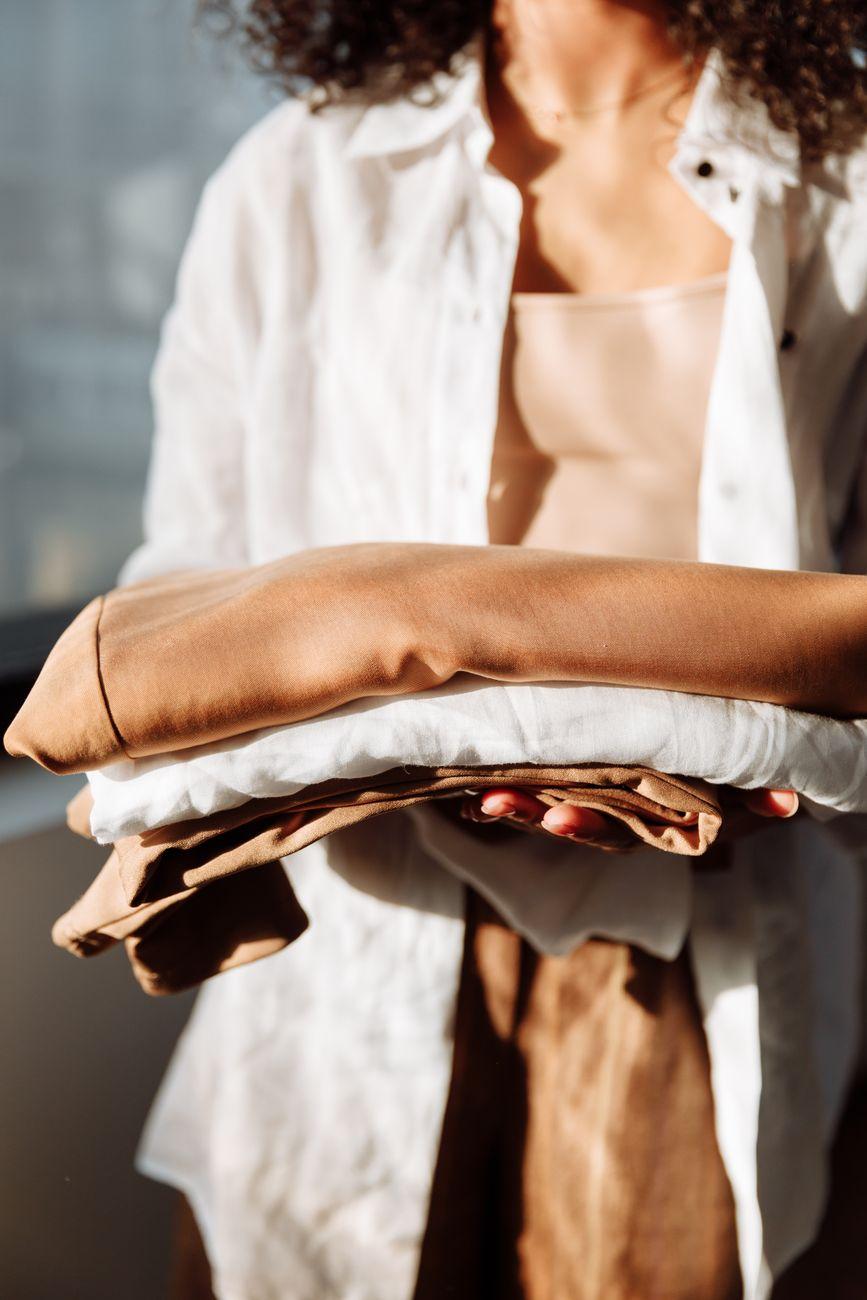 A woman holding neatly folded clothes, bathed in natural sunlight indoors.