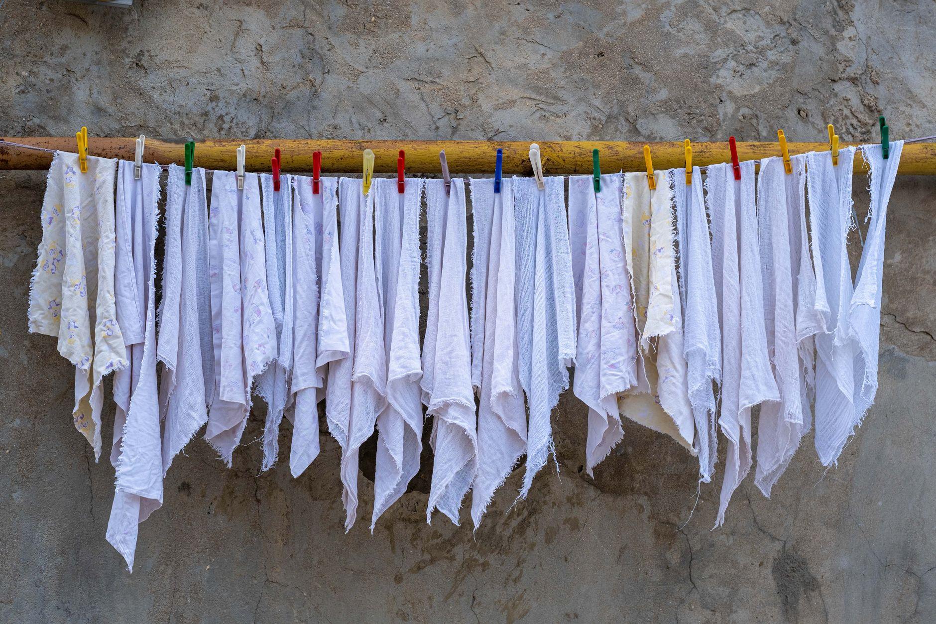 Neatly arranged white fabrics drying under the sun, held by colorful clothespins against a rustic wall.