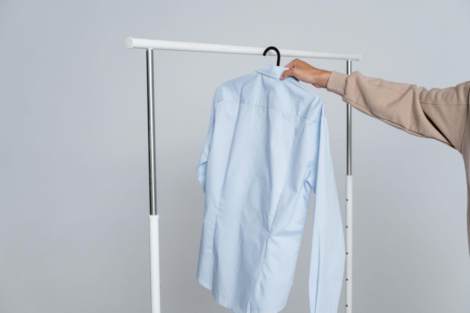 A person holding a blue shirt on a rack against a neutral background.
