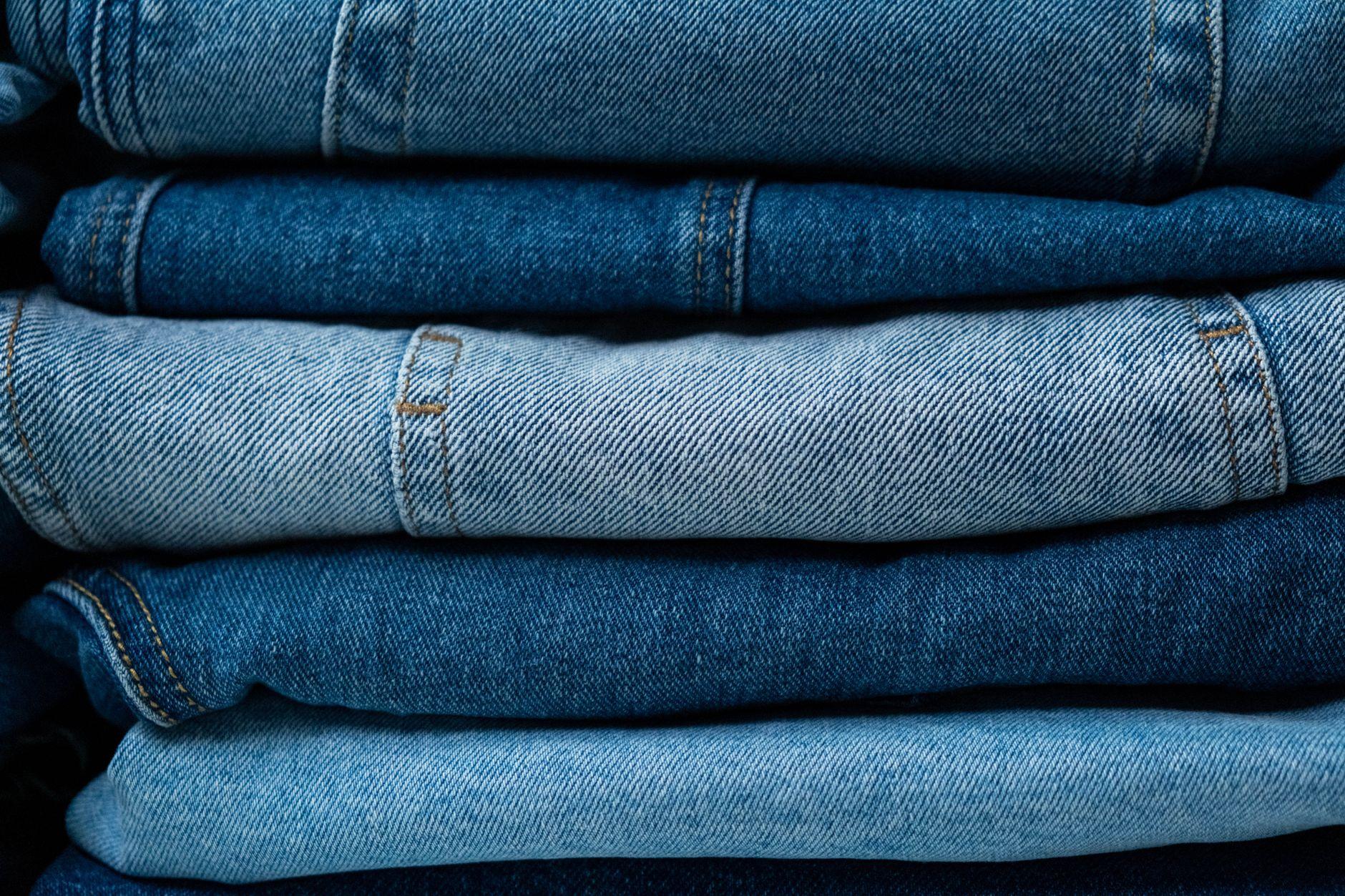 A close-up view of stacked blue denim jeans showcasing various shades of indigo fabric.