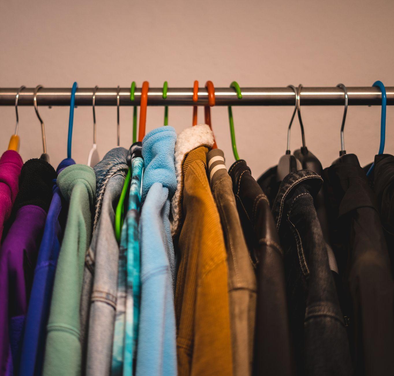 Close-up of various colorful jackets on hangers in a closet setting.
