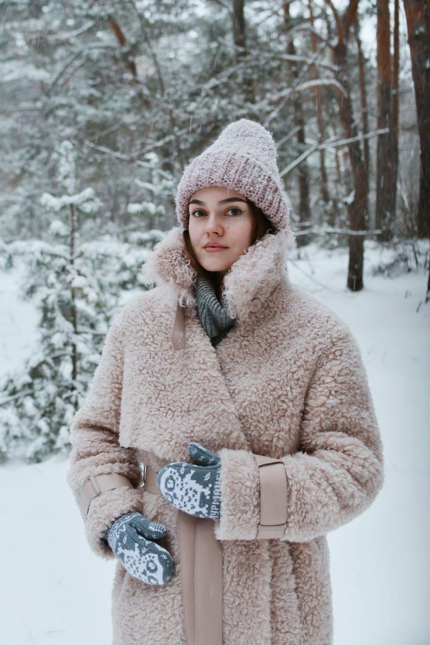 Young woman in stylish winter attire standing in a snowy forest.