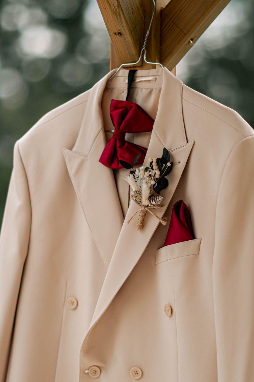 A sophisticated beige suit with a red bowtie and floral boutonniere on display.