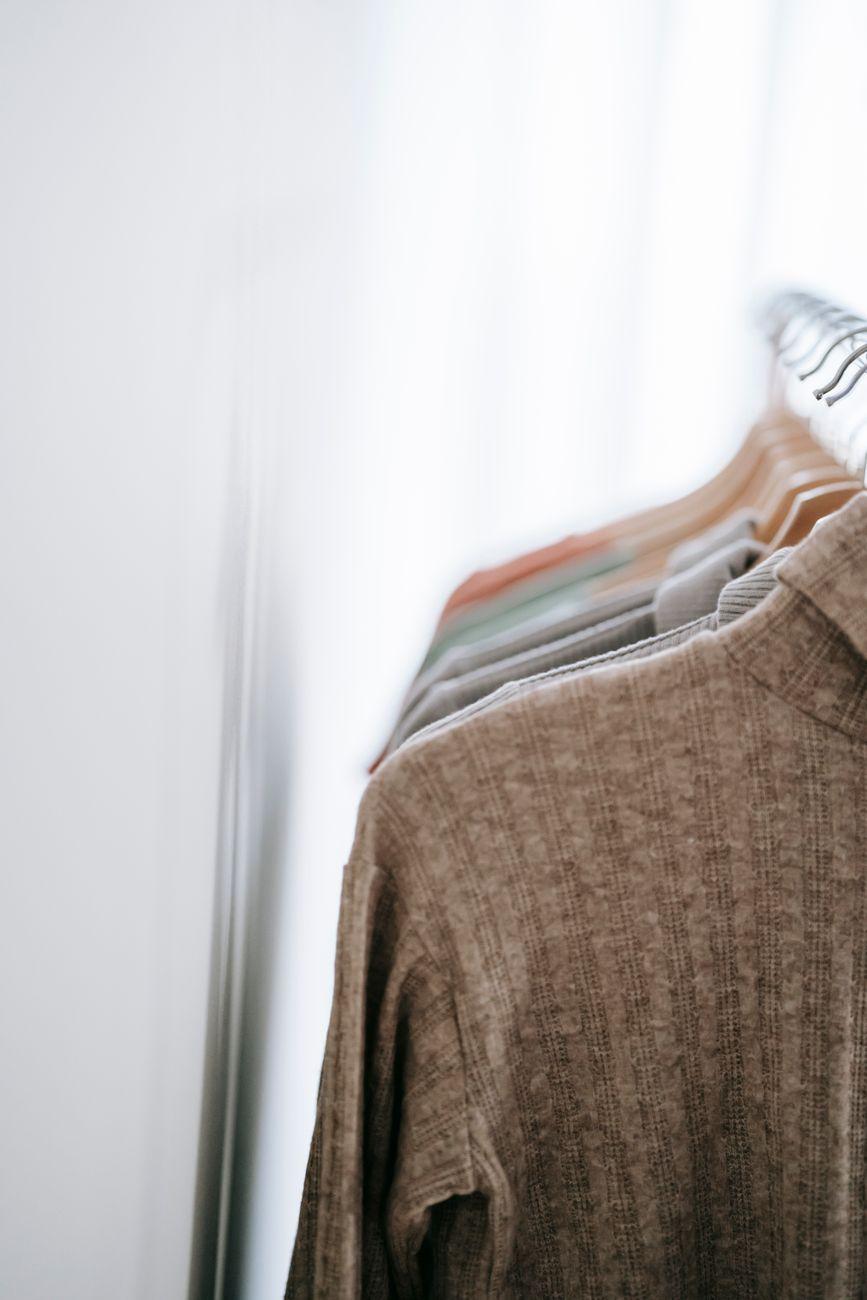 Interior of light room with various clothes on hangers in wardrobe near white walls